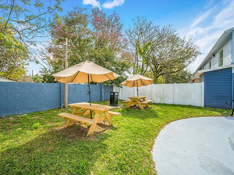Charming outdoor garden with wooden picnic tables and umbrellas, surrounded by lush greenery, perfect for relaxation and gatherings.