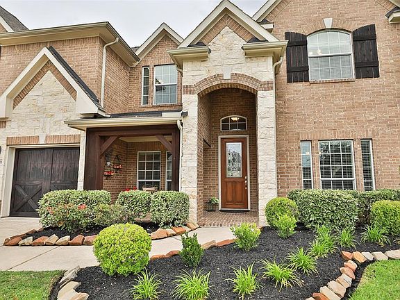 STUNNING CURB APPEAL WITH LUSH LANDSCAPING - This elevation exudes class. Verdant lush landscaping lines the curved sidewalk. To the left, a double-wide driveway with the two cedar wood "barn-like" garage doors with coach lighting. The large back yar