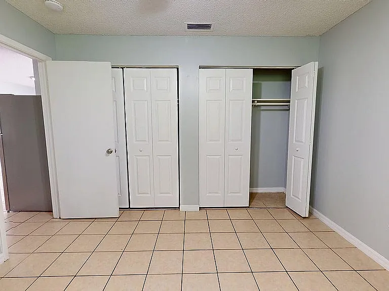 Bright bedroom with sleek tiled flooring, ample closet space featuring dual doors, and freshly painted walls.