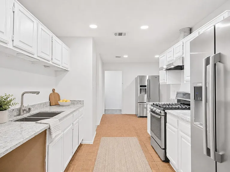 Galley kitchen with stone-look counters, ample cabinetry, and stainless-steel appliances including a gas range and fridge.