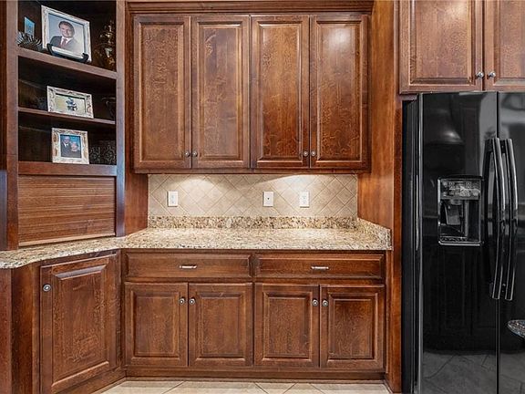 Kitchen with black refrigerator with ice dispenser, decorative backsplash, and light stone countertops
