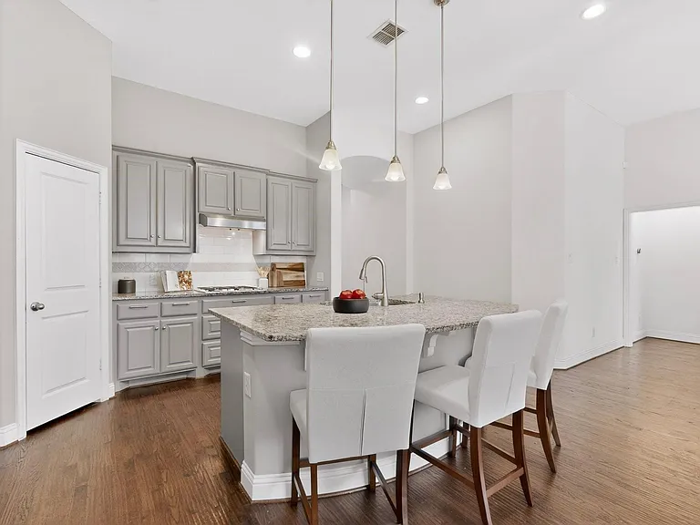 A modern kitchen featuring a kitchen island, stainless steel appliances, warm hardwood floor and decorative lighting, creating a stylish and inviting atmosphere.