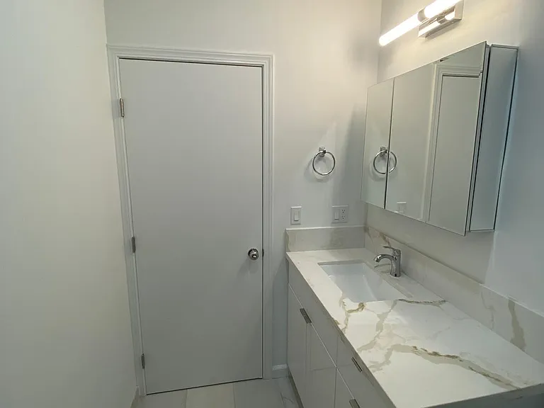 Clean bathroom vanity area with marble-look countertop, modern lighting, mirror cabinet, and bright neutral finishes.