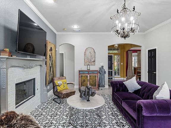 Living area with arched walkways, ornamental molding, a tiled fireplace, and a beautiful chandelier