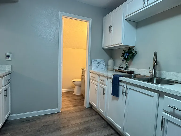 This bright kitchen features crisp white cabinetry, modern fixtures, and a clean layout that flows seamlessly into the adjoining bathroom.