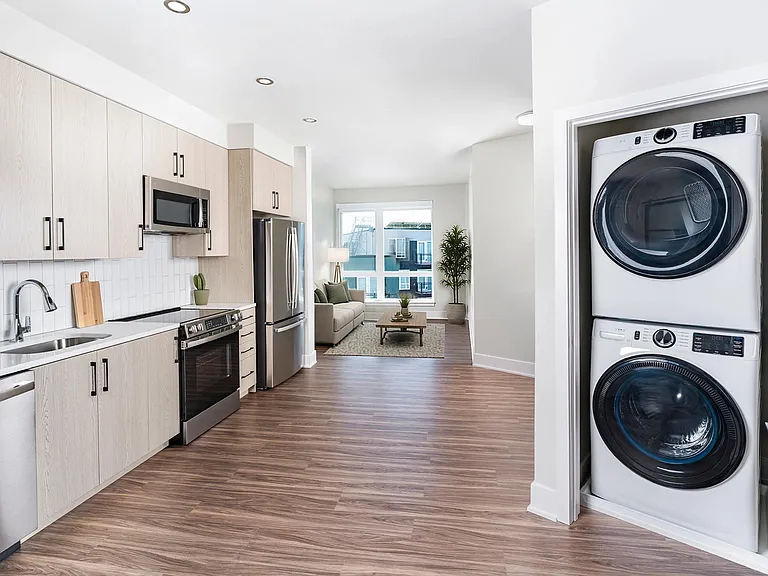 Open kitchen with quartz island seating, light wood cabinetry, and a dedicated in-home laundry closet positioned just outside the primary bedroom.