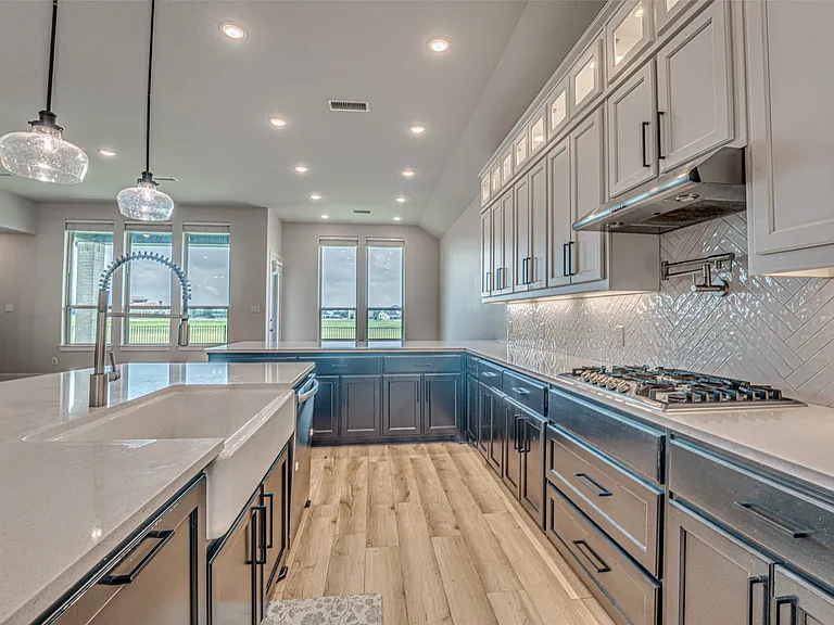 Spacious kitchen featuring a large island with a farmhouse sink, light wood-finish flooring, white countertops, two-tone cabinetry, and a herringbone tile backsplash