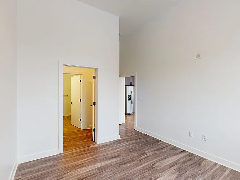 Spacious apartment bedroom with large closet, attached bathroom and wood-style flooring.