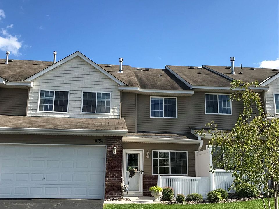 Front of townhouse with asphalt drive, green grass, small enclosed patio.