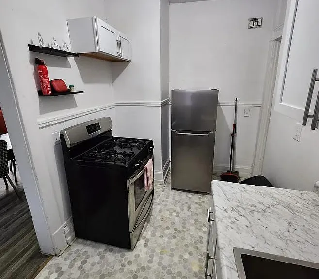 Efficient kitchen with gas range, full-size refrigerator, and marble-look counters plus open shelving for everyday storage.