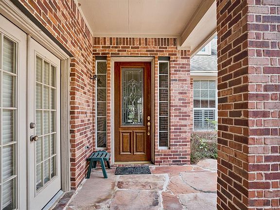 Mature trees surround the home with stacked stone and brick elevation.