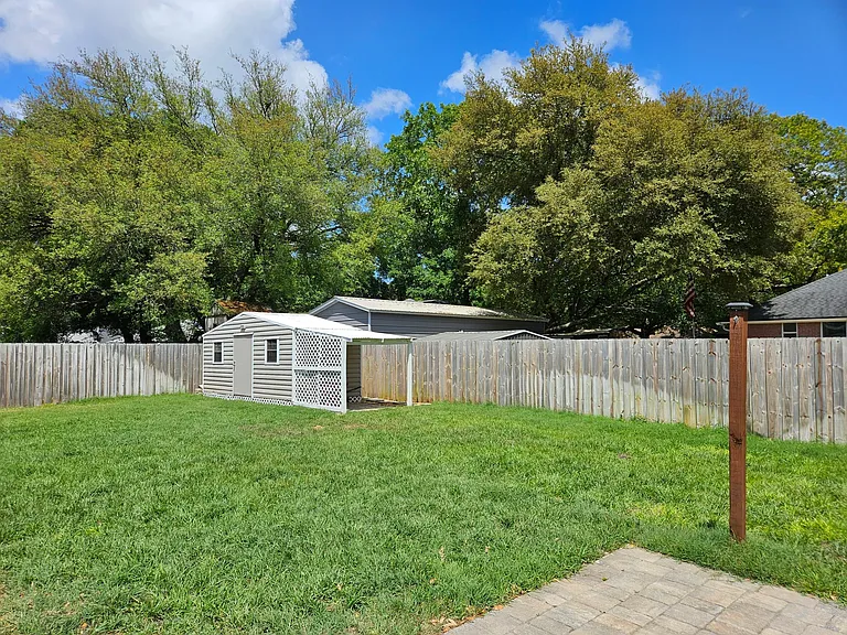 Shed and grass area. Shed has shelving built in and a paver overhang area for parking the mower.