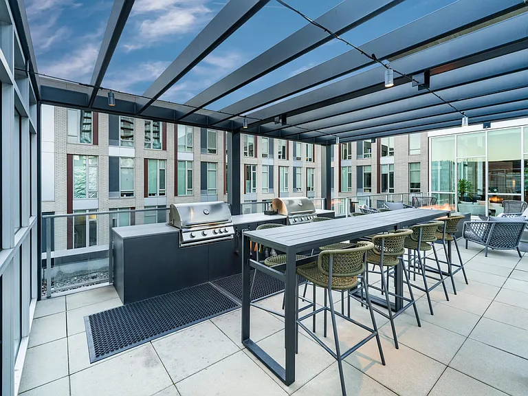 A rooftop grilling area at Modera Pearl with shaded seating and communal tables, designed for hosting meals and casual gatherings above the city.