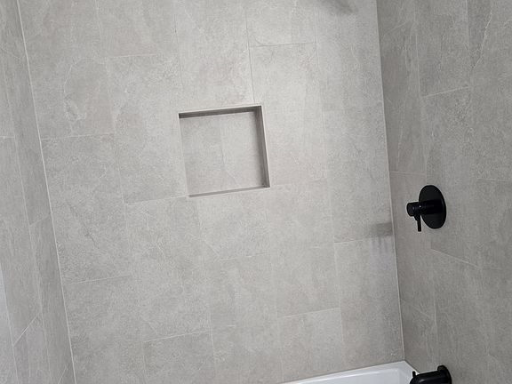 Beautiful, updated bathtub and shower featuring floor-to-ceiling tile, a built in niche and sleek matte black fixtures.