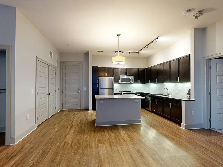 Apartment living room with wood-style flooring and kitchen island (shown here). Kitchen peninsula available in select homes.