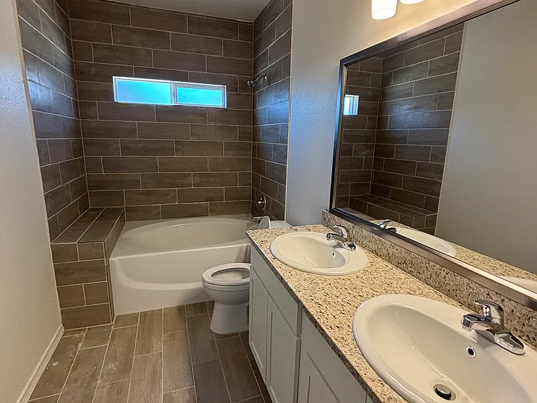 Spacious primary bathroom featuring dual sinks, granite countertops, and a tiled shower/tub combination.