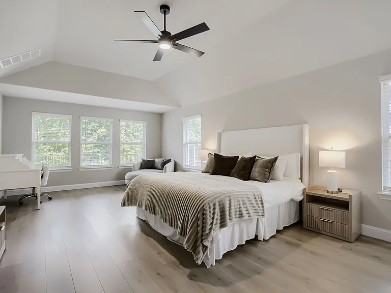 Spacious bedroom featuring vaulted ceilings, light wood-finish flooring, and multiple windows