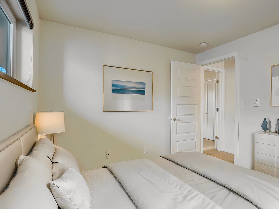 A bright and inviting bedroom featuring a comfortable bed, natural lighting from the window, and a door leading to an adjacent room.