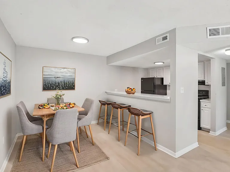 Modern dining area with a stylish table set for four, connected to a chic kitchen with sleek bar seating and contemporary lighting.