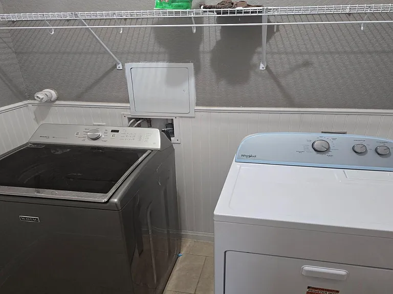 Dedicated laundry nook with washer and dryer, tile flooring, and wire shelving for convenient storage and supplies.