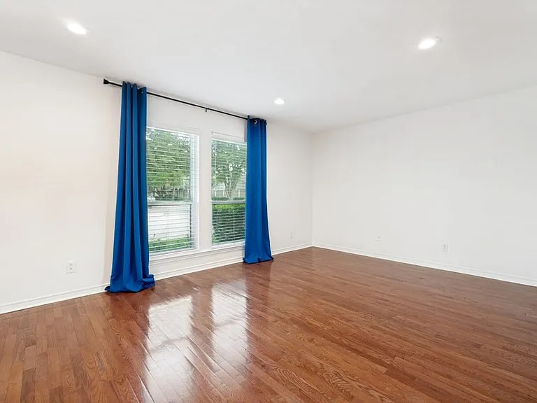 Spacious room featuring wood-finish flooring, white walls, recessed lighting, and two large windows with blinds