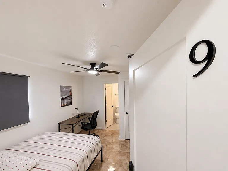 Private bedroom with a large window, ceiling fan, blackout shade, tile flooring, furnished with a large closet and work desk.