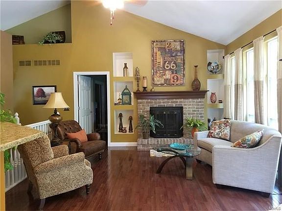 Vaulted great room with woodburning fireplace, wood floors, bookcases & plant shelves.