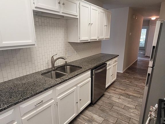 Modern kitchen featuring granite countertops, stainless steel appliances, and white cabinetry. Includes a gas stove, microwave, and spacious refrigerator. Elegant tile flooring and ample storage space create a functional and stylish cooking area.