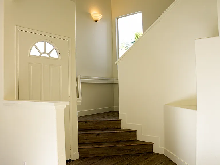Staircase by the entry door finished in laminated vinyl plank with new baseboards.