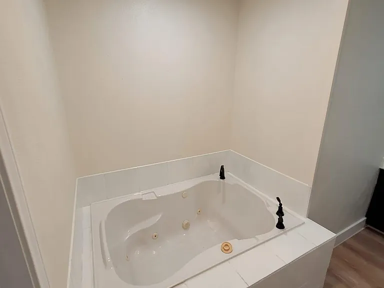 Relax in a jetted soaking tub with tile surround and updated fixtures, set beside durable wood-look flooring.