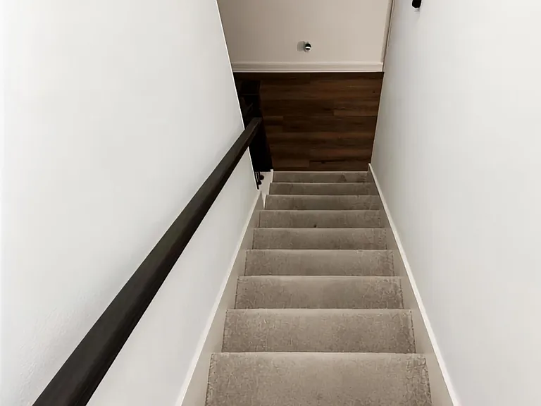 Carpeted stairwell with sturdy handrail leads to a landing with wood-look flooring, offering easy access between levels.