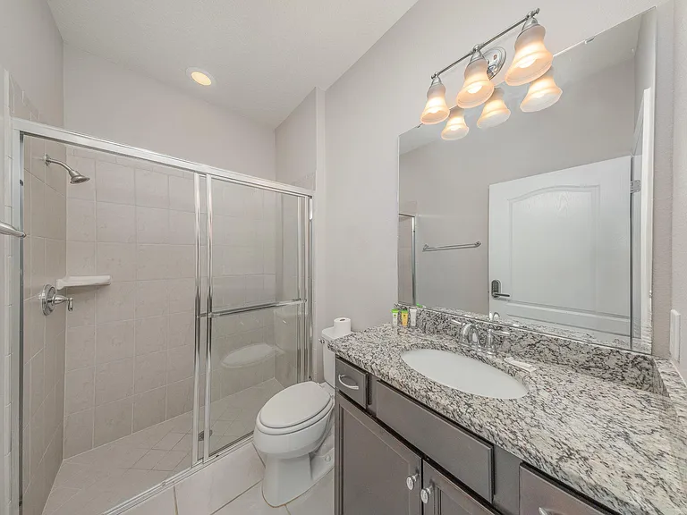 Modern bathroom with granite countertop and walk-in shower featuring glass doors.