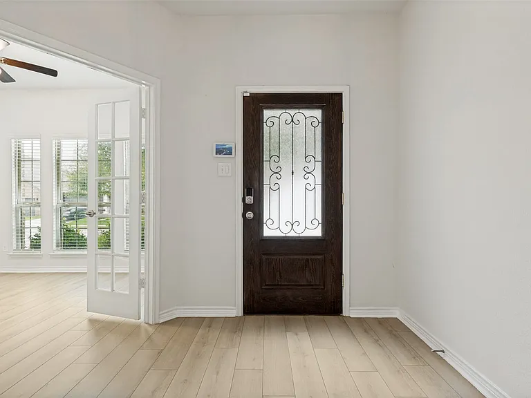 Entryway featuring a dark wood-finish door with decorative ironwork and frosted glass, light wood-finish flooring, white baseboards, and a contemporary smart thermostat