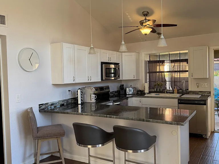 Updated kitchen with bar seating, ample white cabinetry, and stainless appliances, plus a sink window and pendant lighting.