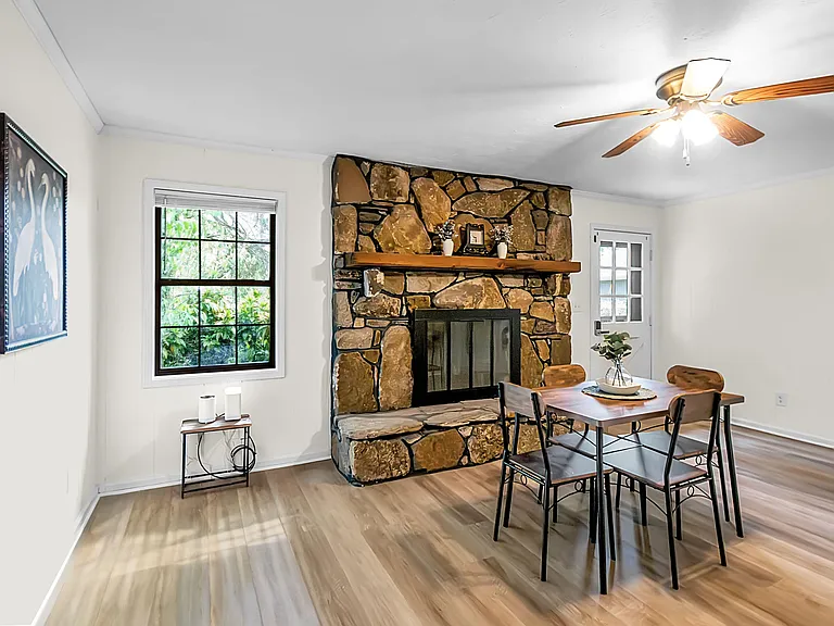 Dining area with a stone fireplace centerpiece, ceiling fan, and nearby window, plus space for a full dining set.