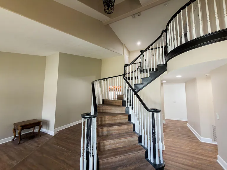 Open entryway with a sweeping curved staircase, high ceilings, and durable wood-style flooring connecting to main areas.
