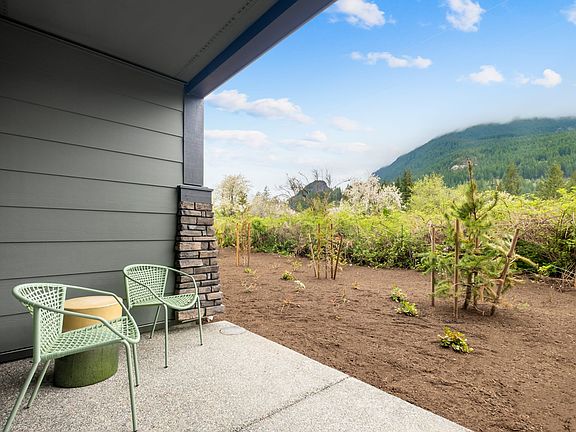 A cozy outdoor seating area with green chairs overlooking a lush, mountainous landscape with a cloud