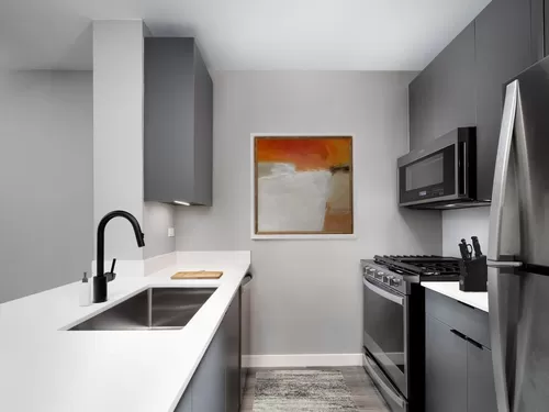 Renovated Package II kitchen with white quartz countertop and backsplash, upgraded stainless steel appliances, upgraded black hardware, and upgraded lighting - Avalon Midtown West