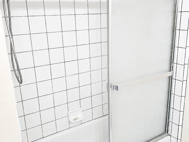 Second bathroom with tub/shower combo, tile surround, and sliding glass shower door.