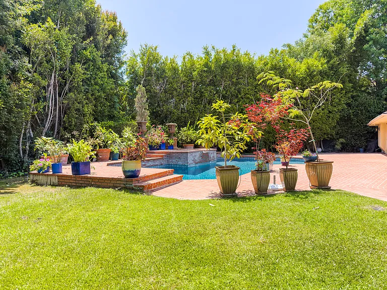 Colorful potted plants line the lawn beside this inviting pool at this Beverly Hills luxury rental, 1094 Garden Lane, 90210.