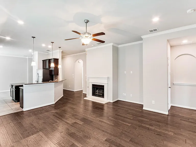 Open-concept living space with dark wood-finish flooring, a central fireplace, and a ceiling fan