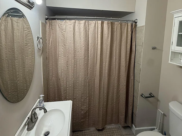 Full bathroom with a vanity sink, wall mirror, shower/tub combo with curtain, and an over-toilet wall cabinet for storage.