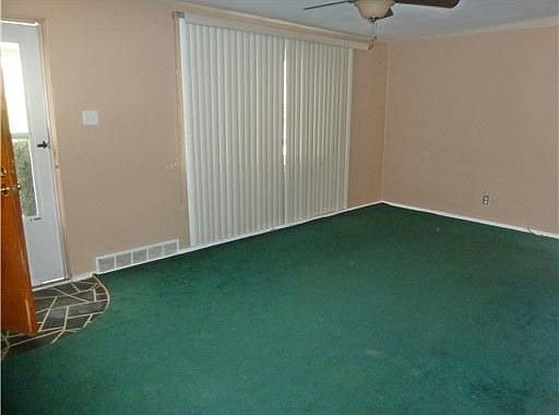 The living room features wall-to-wall carpeting, ceiling fan & vertical blinds