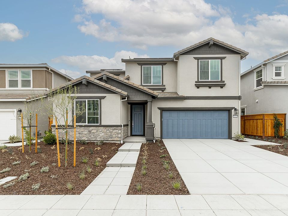 A modern two-story residential house with a garage, surrounded by a paved driveway and landscaped ya
