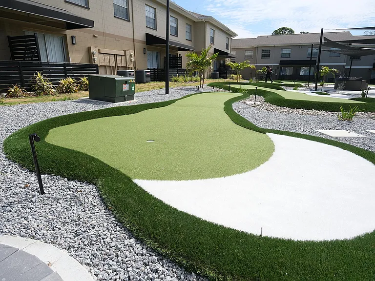 Beautiful apartment courtyard featuring a modern mini-golf green surrounded by manicured grass and stylish landscaping.