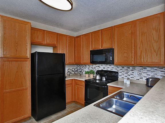 Kitchen featuring all black appliances, large Formica counter tops, and walnut cabinets.