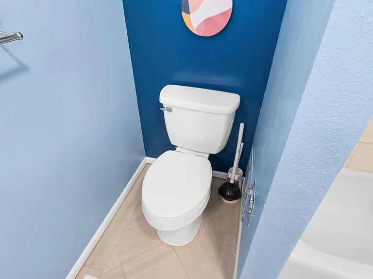 Half bath with tile flooring, a standard toilet, and towel bar, set off by a bold accent wall for added character.
