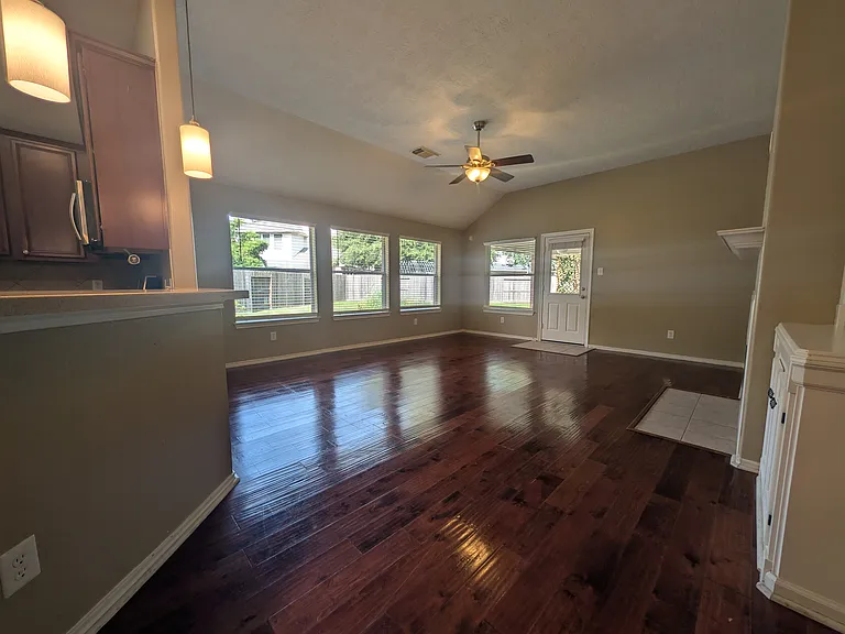This wide view showcases the massive open-concept living space, complete with dramatic vaulted ceilings, a ceiling fan, and rich, deep-toned wood-look flooring that spans the entire room.