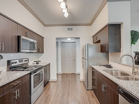 Open kitchen with granite countertops, stainless steel appliances and dark cabinets overlooking separate dining area