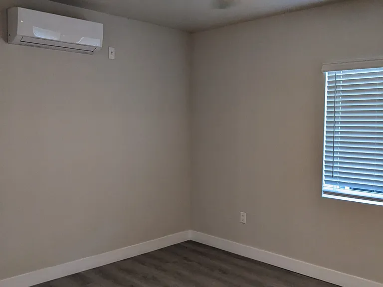 Bedroom with large window, ceiling fan, and air conditioner at The Hardison Apartments in Pasadena, California.